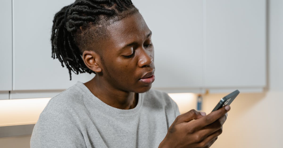 Young man with braided hair checking his smartphone while at home, embodying modern lifestyle.