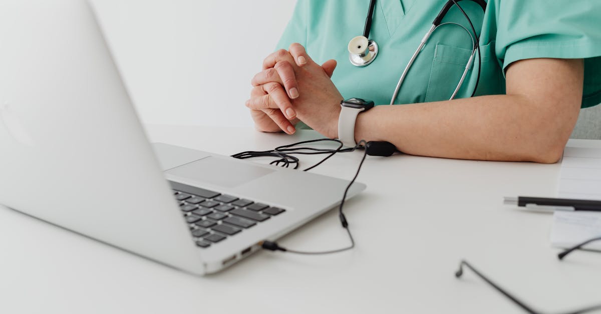 Medical practitioner in scrub suit using a laptop for remote consultation and documentation.