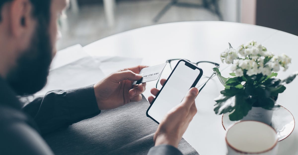 A man holding a credit card and smartphone at a table, engaging in online payment indoors.