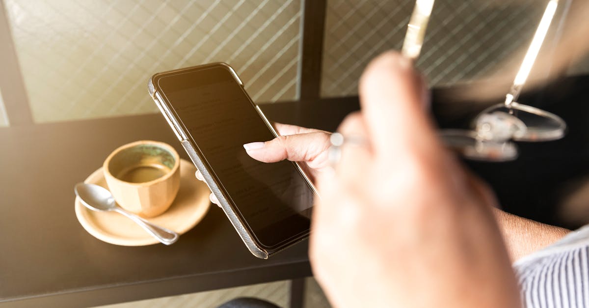 Person checking smartphone next to coffee on table, indoors.