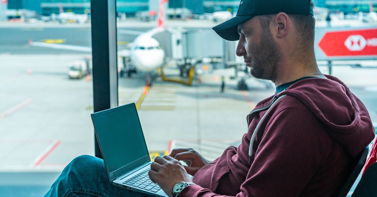 A man working on his laptop in an airport terminal, with a plane visible outside.