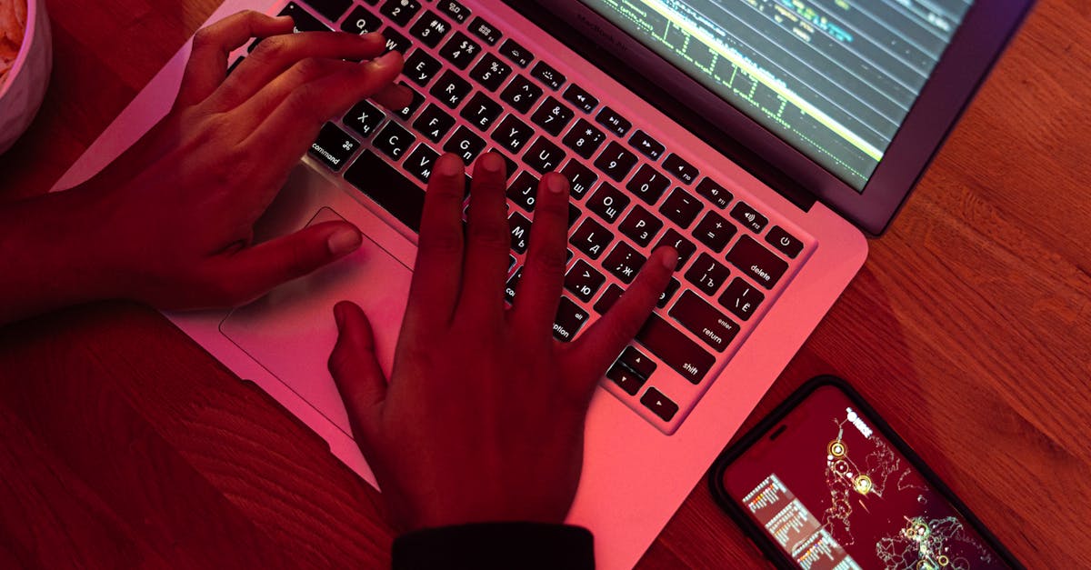 Hands typing on a laptop with code on screen, smartphone nearby at night, indoor setting.