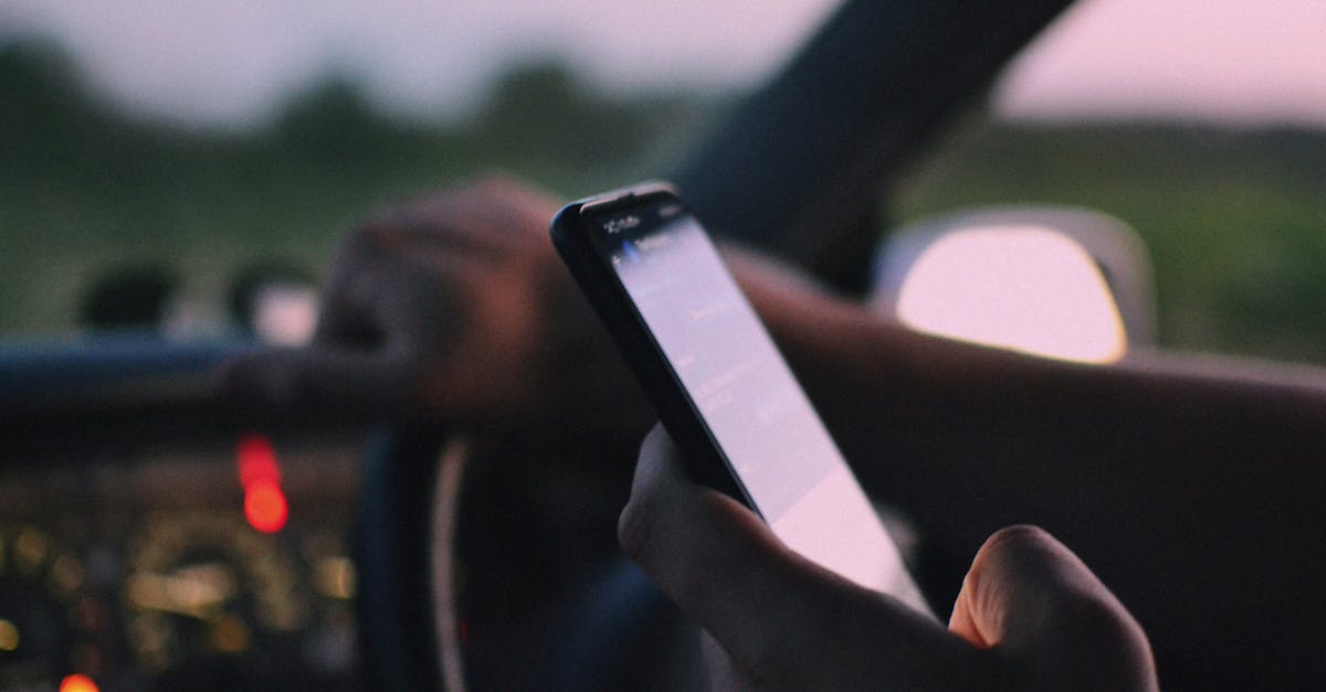 Close-up of a person using a smartphone while driving in a car at dusk.