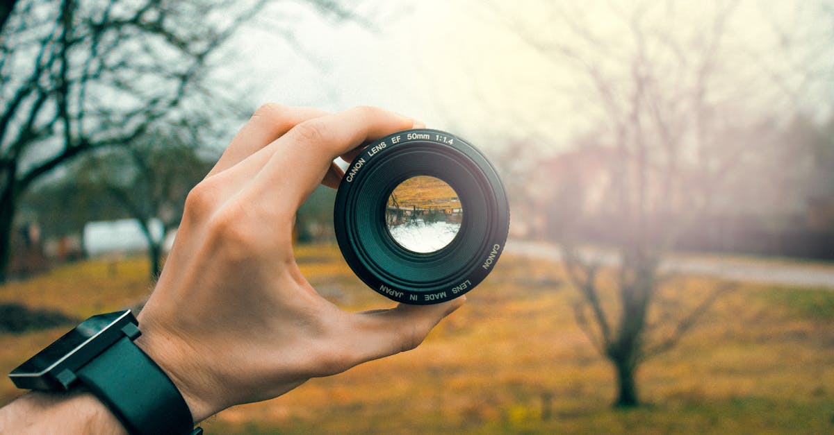 Close-up of a hand holding a 50mm camera lens outdoors, focusing through the lens.