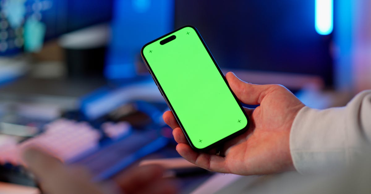 Hand holding a smartphone with a green screen in a modern indoor setting, ready for app design or mockup.