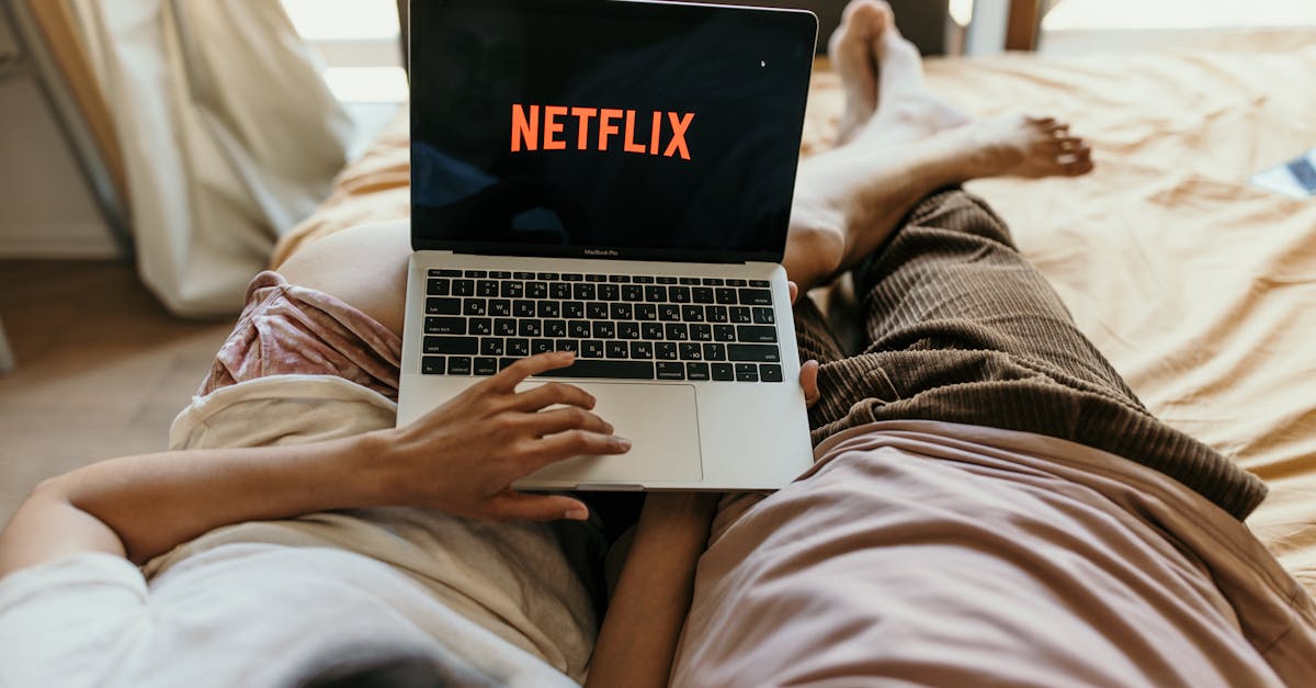 A couple lying comfortably in bed watching Netflix on a laptop, enjoying leisure time together indoors.