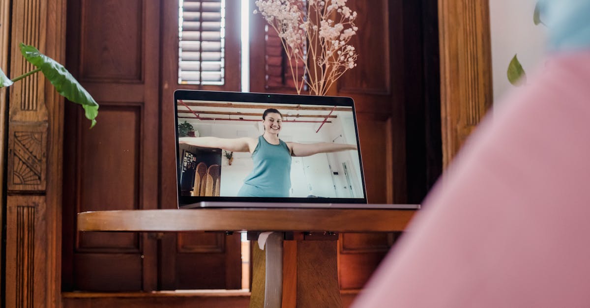 A woman engages in an online yoga session via laptop in a cozy home setting, focusing on wellness.