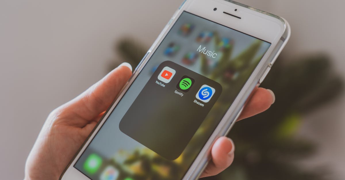 Hand holding a smartphone displaying popular music apps like Spotify and Shazam in a close-up shot.