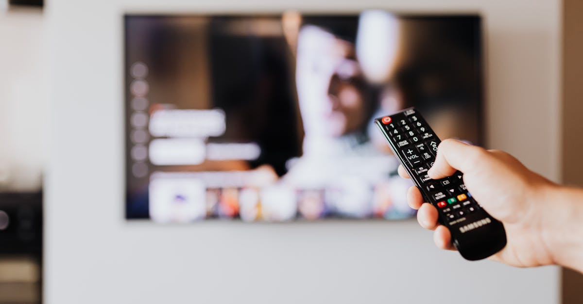 Person using a TV remote control with a blurred television screen in the background.