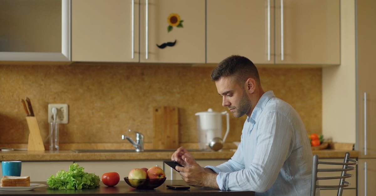 Man browsing smartphone in a modern kitchen with fresh produce on the table.