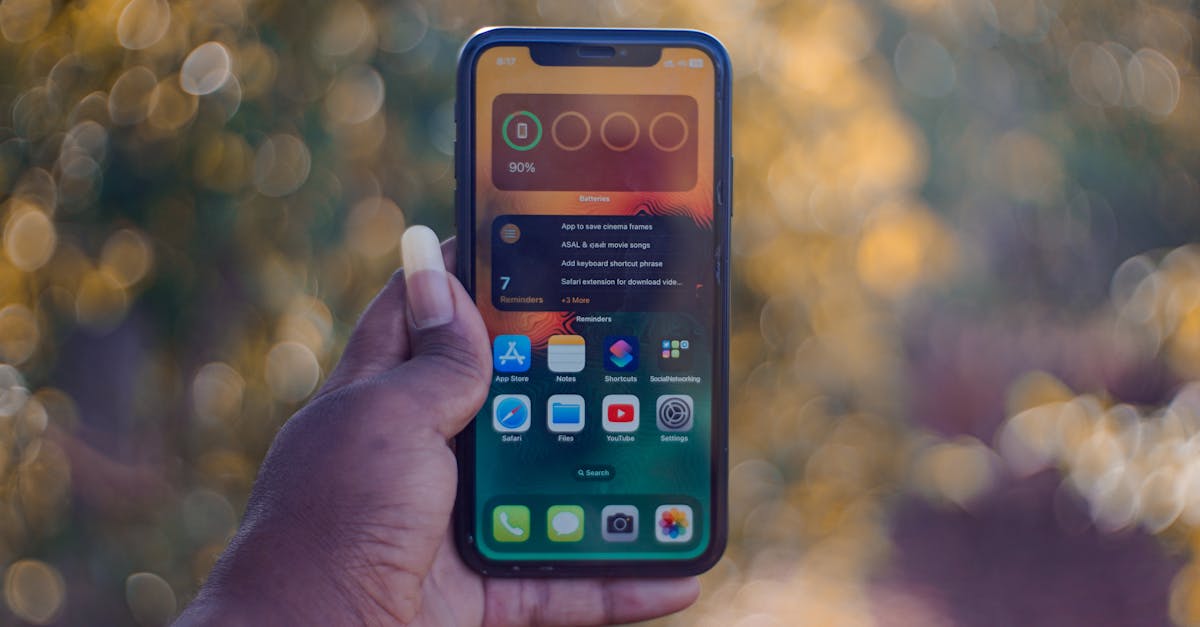 A hand holding a smartphone showing home screen apps, outdoors with bokeh background.