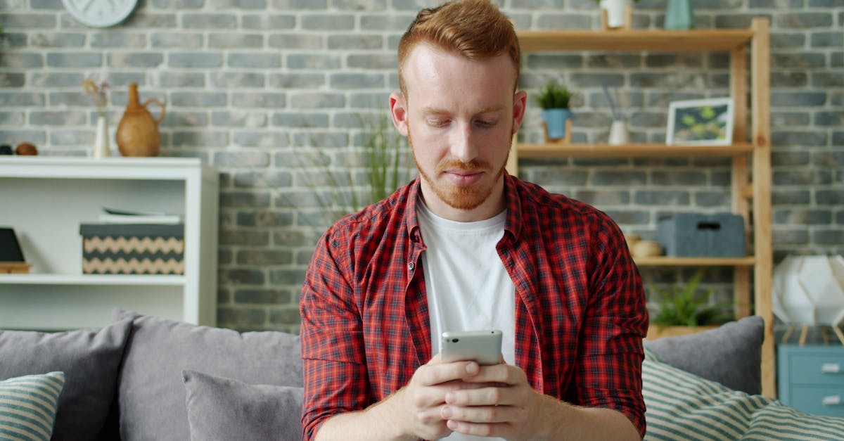 Man in red plaid shirt texting on smartphone at home, modern lifestyle.