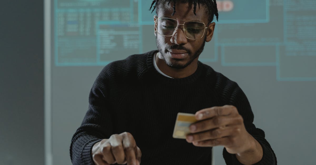 Man with glasses holding a bank card while typing on a keyboard, sitting in front of a computer.