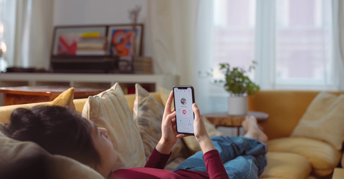 Woman relaxing and using a dating app on her smartphone while lying on a sofa indoors.