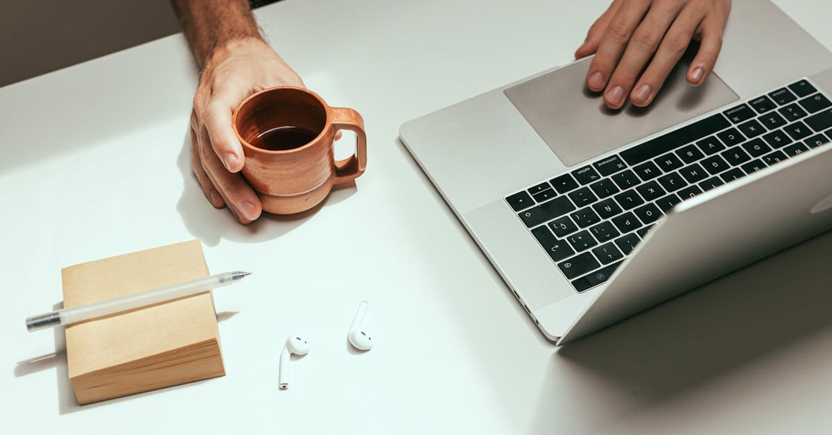Minimalist workspace featuring a laptop, coffee mug, and AirPods for a modern work setup.