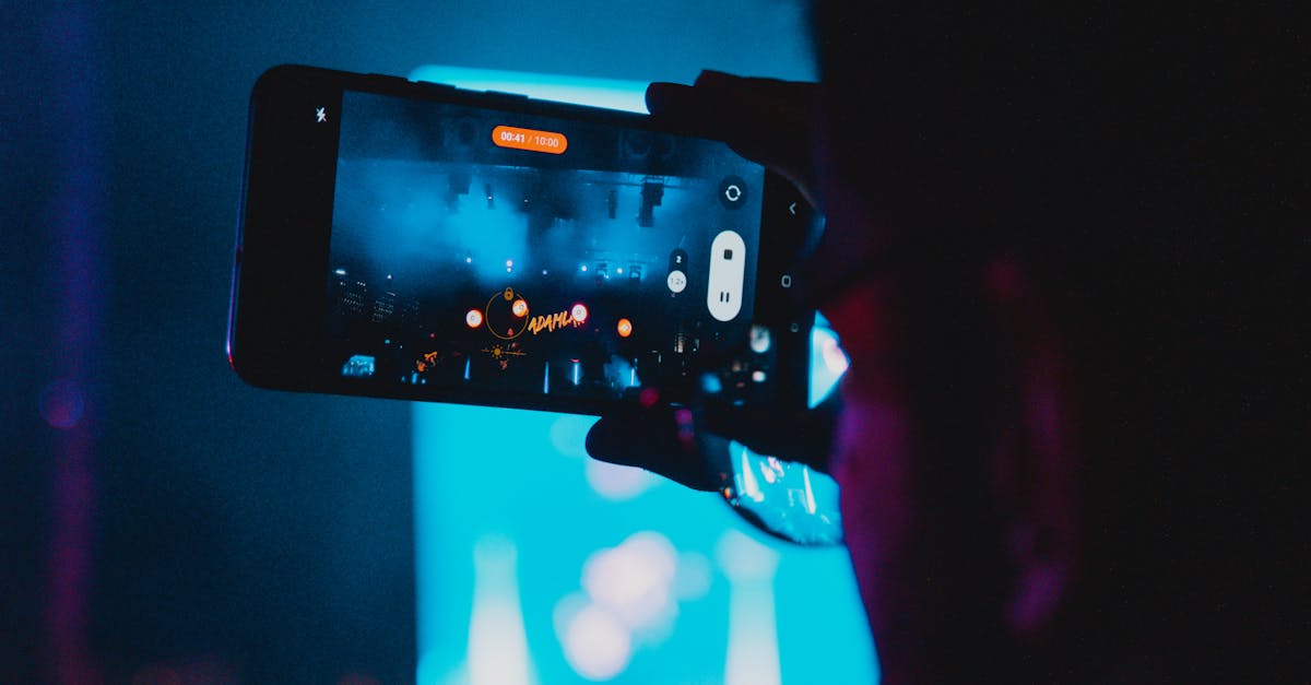 Close-up of a person filming a concert with a smartphone, capturing vibrant stage lights and atmosphere.